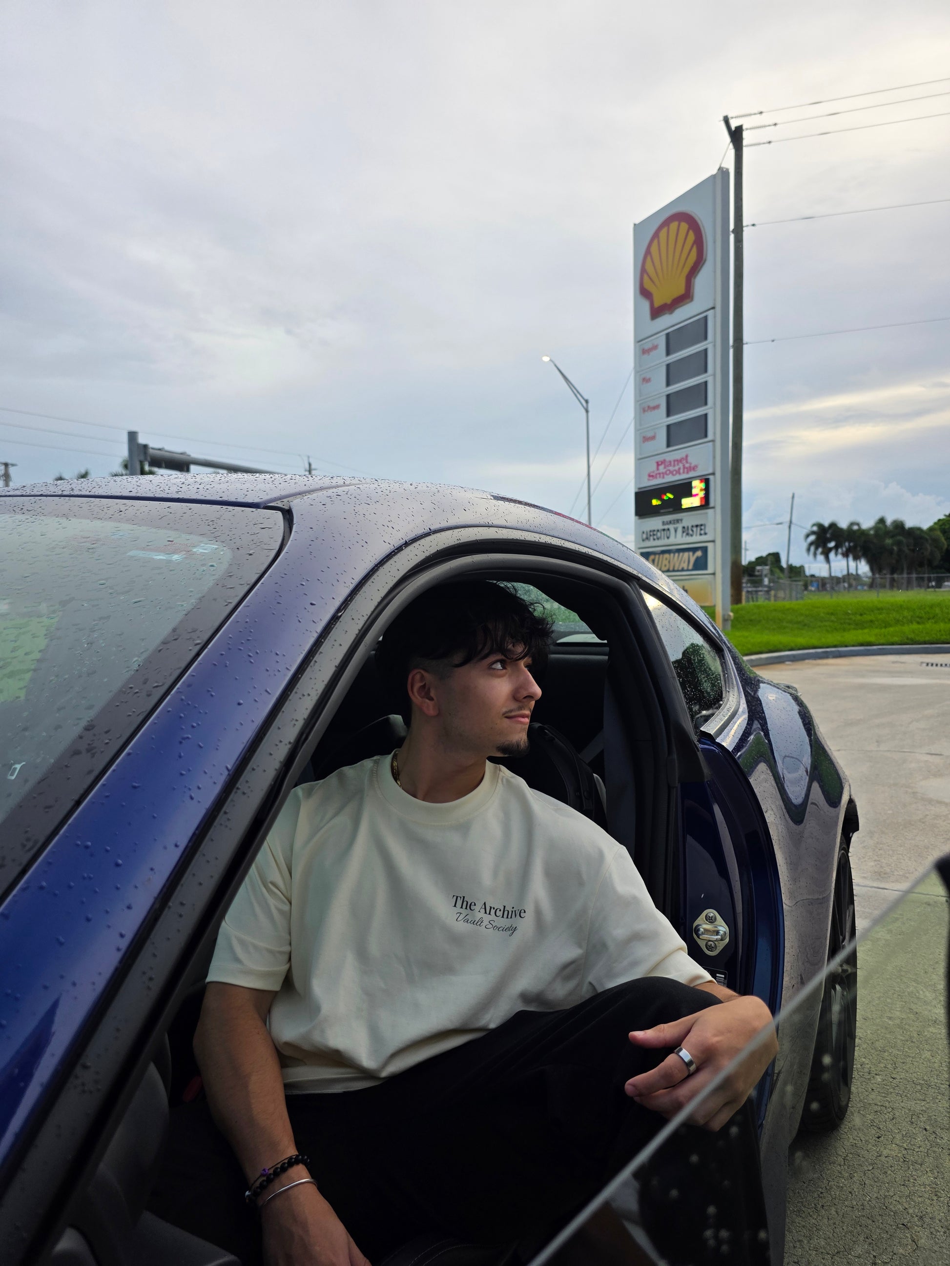 Person sitting inside a car at a gas station with a Shell sign in the background