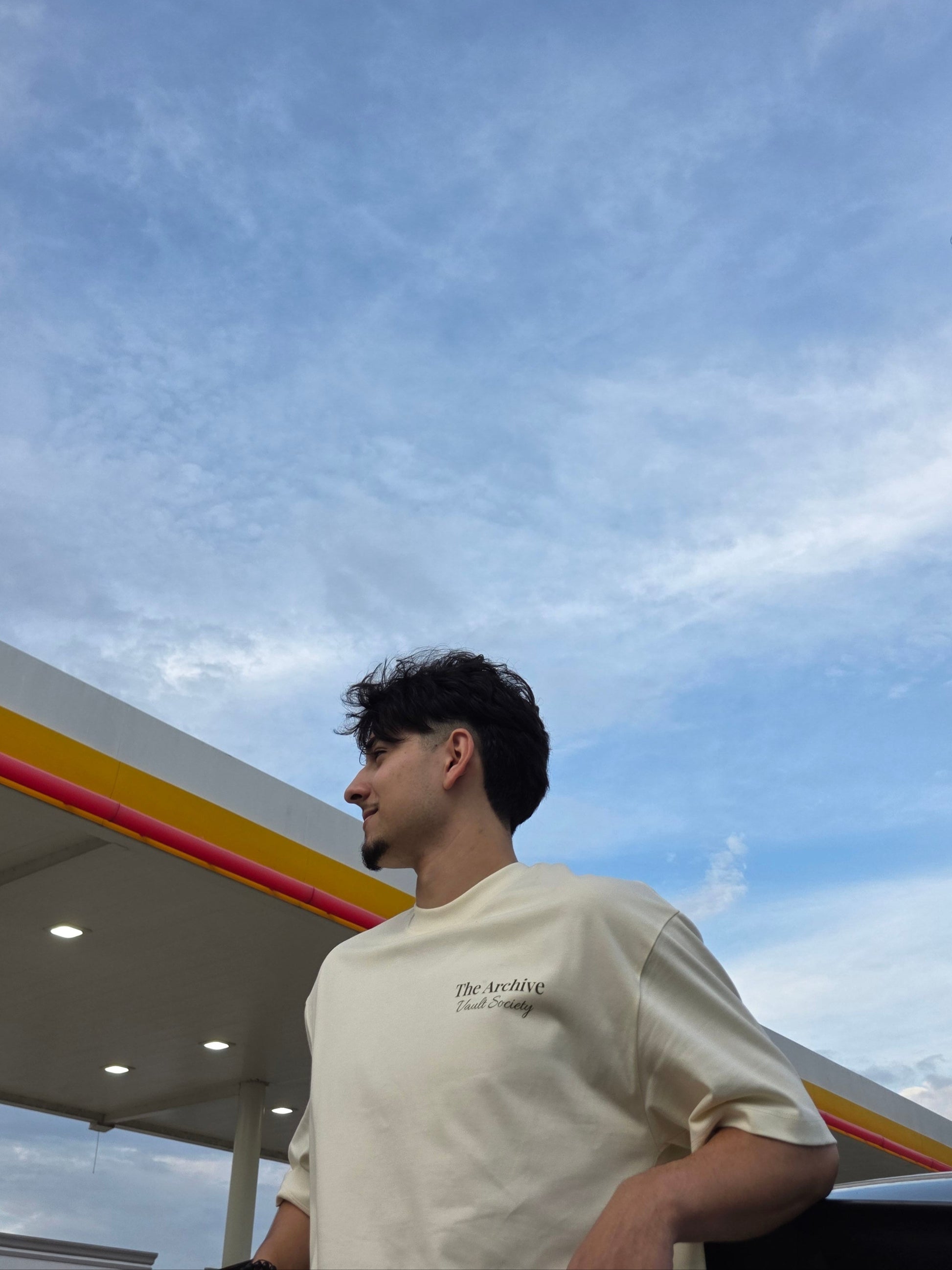 Person standing under a clear blue sky with a gas station in the background